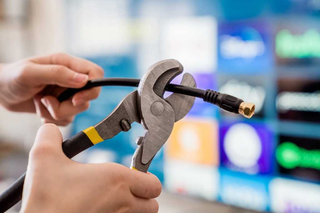 Coax cable being cut in front of a TV with streaming apps